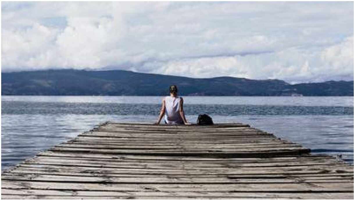 Person sitting on a wooden pier looking out over a lake